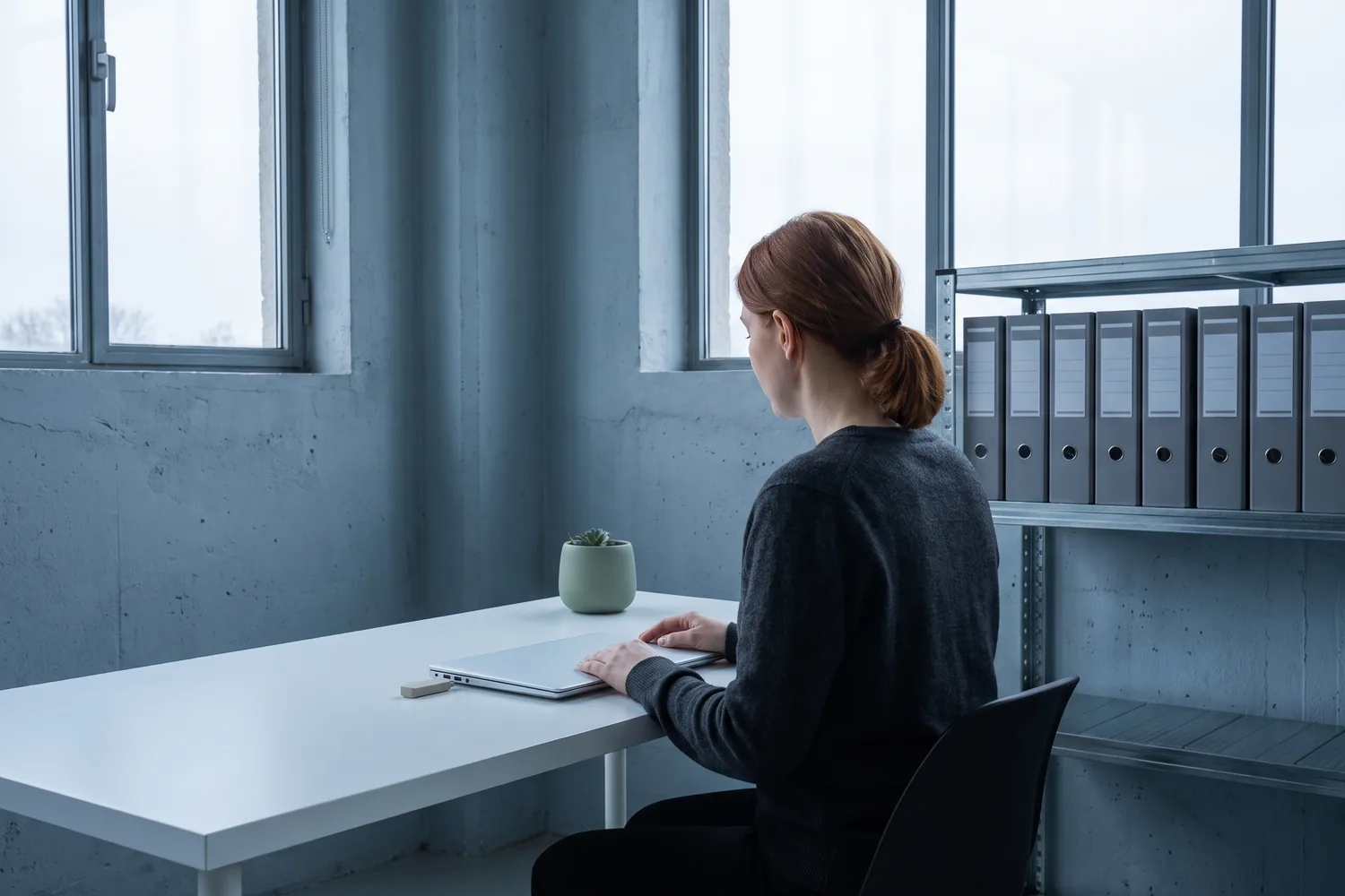 An investor at a desk beside a shelf of identical archive binders, a drive plugged into her laptop.
