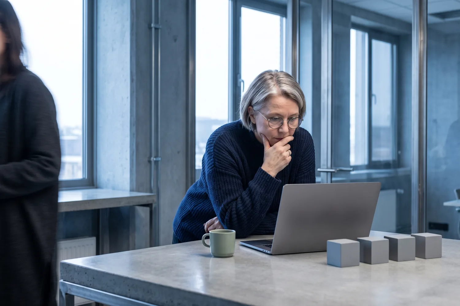 An investor leaning in to her laptop, four identical blocks lined up beside it.