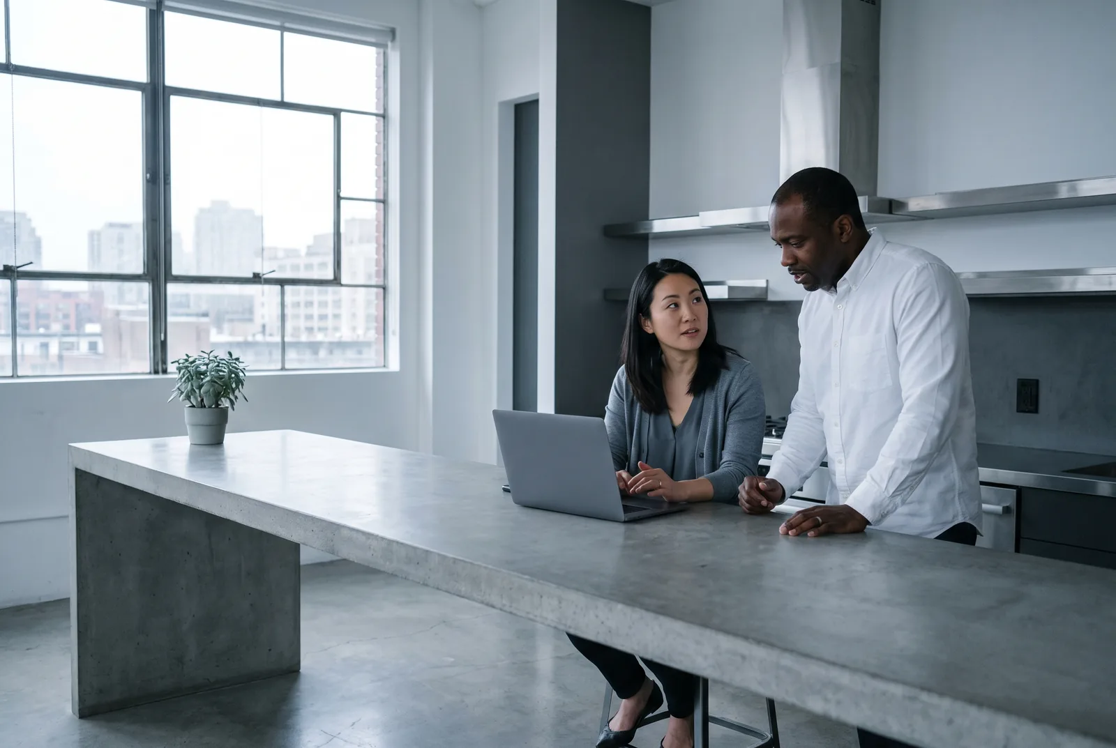 Two investors talking over a laptop at a concrete kitchen island in daylight.